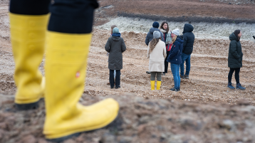 Eine Gruppe in einem trockenen Flussbett und Gummistiefel im Vordergrund