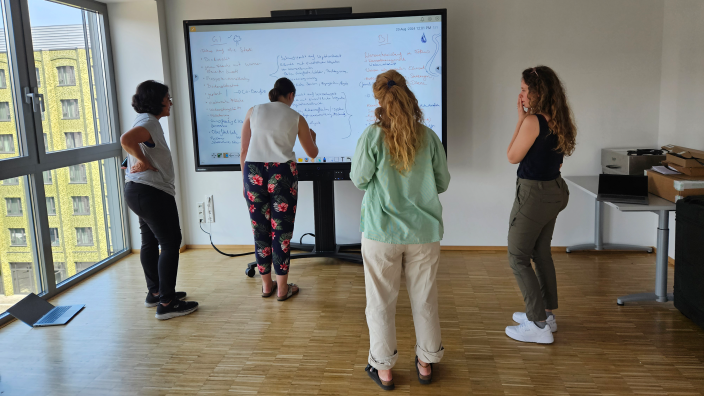 Vier Personen stehen vor einem Whiteboard