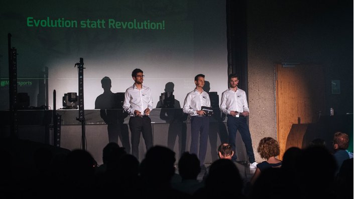 Drei junge Männer auf der Bühne vor dem Motto: "Evolution statt Revolution!".