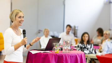 Eine Frau steht an einem Stehtisch und hält eine Ansprache.