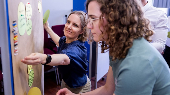 zwei Frauen pinnen Notizzettel an eine Metaplanwand