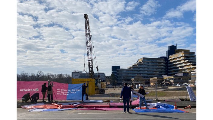 Mitarbeitende der TH Köln und des BLB befestigen 50 Banner an den Bauzäunen