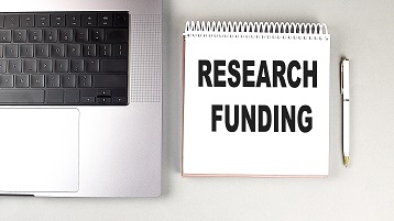 Notizblock, auf dem "Research Funding" steht, neben einem Stift und einem Laptop (Image: AdobeStock / Iryna)