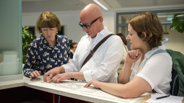 zwei Personen testen mit Oberbürgermeisterin Henriette Reker eine Wegweisertafel in Brailleschrift (Bild: Constantin Ehrchen)