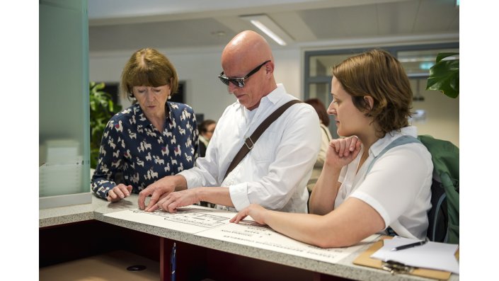 zwei Personen testen mit Oberbürgermeisterin Henriette Reker eine Wegweisertafel in Brailleschrift