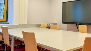 Blick in den Gruppenraum. Zu sehen sind Tische und Stühle und das Smartboard an der Wand (Bild: TH Köln/ Alina Beier)