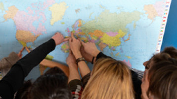Studierende zeigen mit den Fingern auf einer Weltkarte auf ihre Heimatländer (Image: Costa Belibasakis/FH Köln)