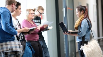 Eine Studentin mit Notebook steht vor einer Gruppe anderer Studierender (Bild: Thilo Schmülgen/FH Köln)