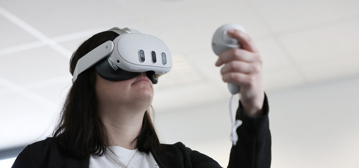 Eine junge Frau trägt eine VR-Brille und hält einen zugehörigen Controller in der Hand. (Bild: TH Köln)